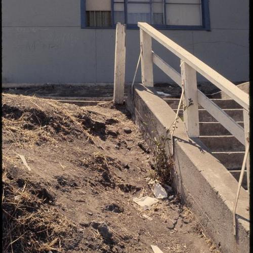 Withered hillside in front of apartment with damaged stair railing