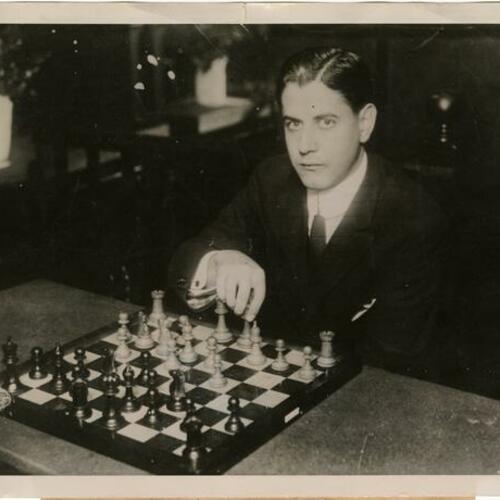 Chess champion Jose Capablanca sitting at chessboard with hand on chess piece