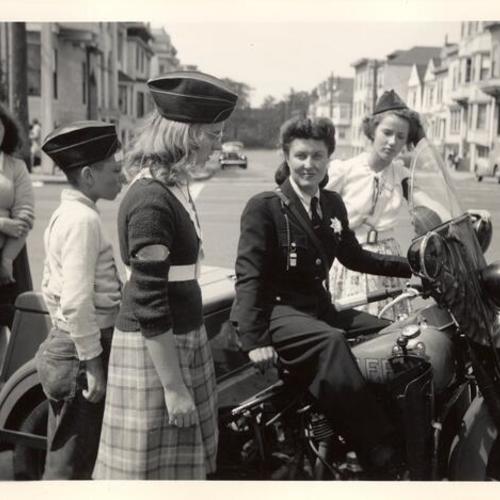 [Patrolwoman sits on her three wheeled motorcycle while talking with young people]