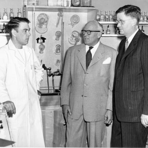 [Laboratory technician Arnold Harrington giving a tour of his work place in the Stonestown Medical and Dental Center to builder Henry Stoneson and San Francisco Public Health Director Dr. Ellis D. Sox ]