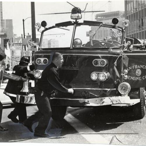 [Firemen pushing damaged truck out of the way of traffic after a collision between a fire engine and a car at Van Ness Avenue and Hayes Street]