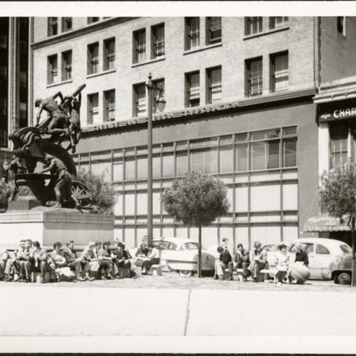 [Group of people sitting around the base of the Donahue Monument, also known as the Mechanics Monument, on Market Street]