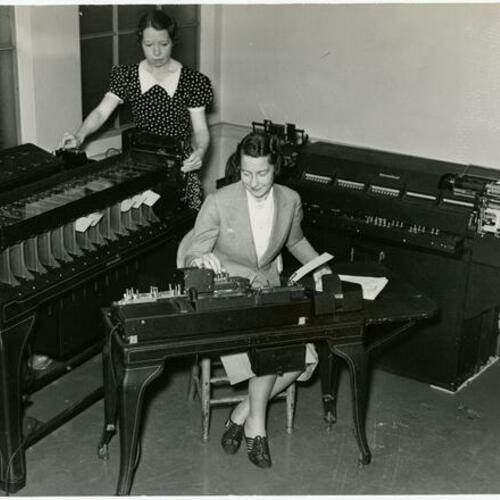 [Mrs. Eleanor Brooks and Miss Virginia McCarthy working on San Francisco police crime investigation machine.]