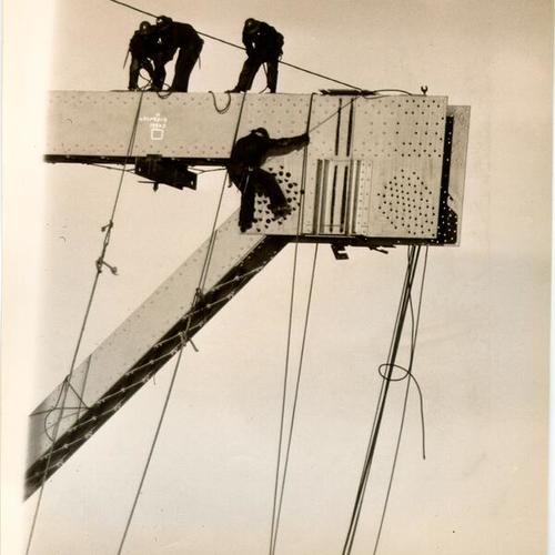 [Workers positioning a large steel structure during construction of the San Francisco-Oakland Bay Bridge]