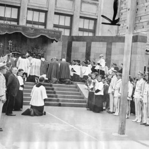 [Church leaders kneeling in prayer at outdoor altar during novena to St. Anne]
