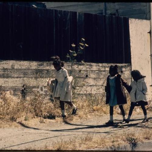 Three children walking along sidewalk