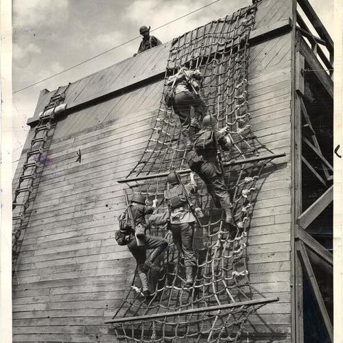 [Four soldiers coming down the side of a mock-up ship as part of a training exercise]
