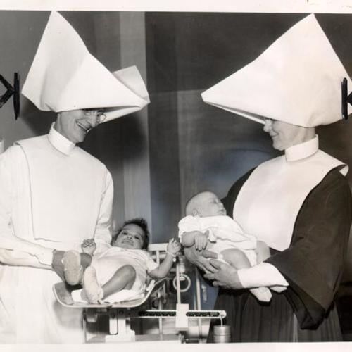 [Sister Ann Elizabeth and Sister Celestine preparing to check the weights of two babies at St. Elizabeth's Infant Shelter]