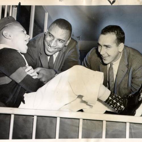 [Football players Curtis McClinton and John Hadl visiting with an eight-year-old patient at the Shriners' Hospital for Crippled Children]
