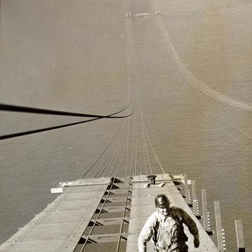 [Workman walking up the catwalk construction of Golden Gate Bridge]