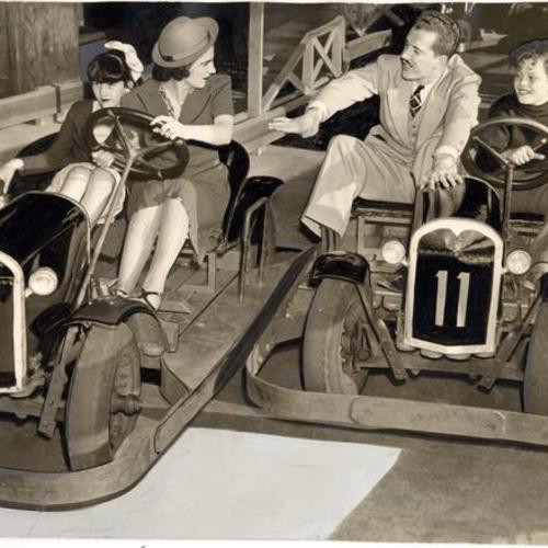 [Pat Dugan, Carla Rossi, Ross Stevens and Mike Dugan riding electric automobiles at Playland at the Beach]