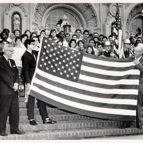 [Group of people posing with an American flag on the steps of Mission High School]
