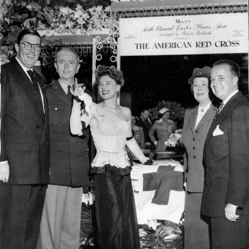 [Five people standing in front of a Red Cross "wishing well" during a preview of Macy's annual Easter flower show]