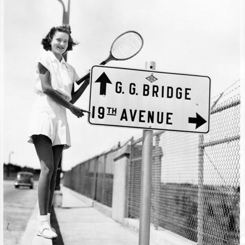 [Marilyn Castillo pointing at traffic sign which shows direction to Golden Gate Bridge and 19th Avenue]