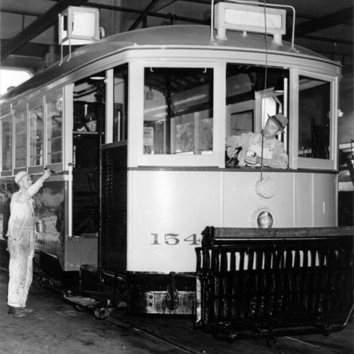 [Workers repainting a streetcar in the Municipal carbarn at Geary Boulevard and Presidio Avenue]