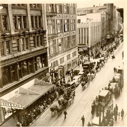 [Parade of horse drawn carriages passing by the "Carriage Entrance" to Roos Brothers' store]