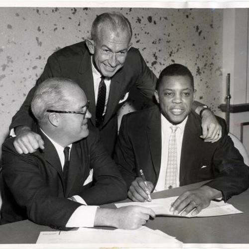 [Willie Mays signing the contract as the highest paid player in baseball in front of Giants President Horace Stoneham and Manager Bill Rigney]