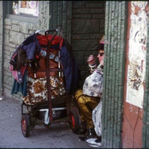 [Person sits in doorway with belongings on cart]