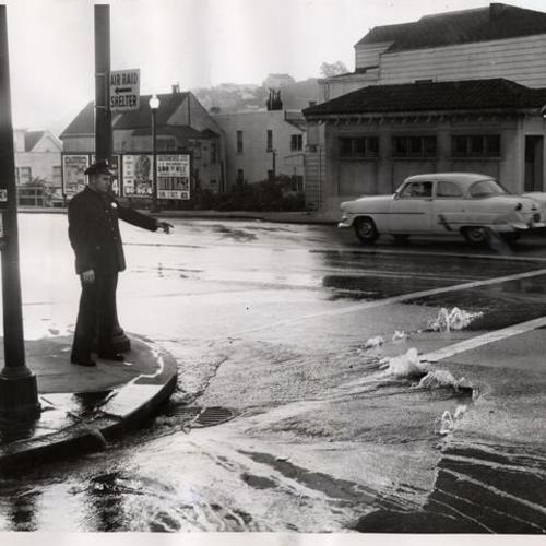 [Officer Charles McLaughlin from Mission station pointing at a broken water main at the corner of Eureka and Market streets]