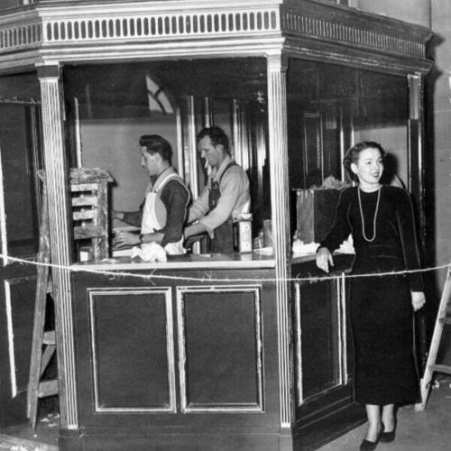 [Betty Gassman and two workers standing at the information booth in City Hall]