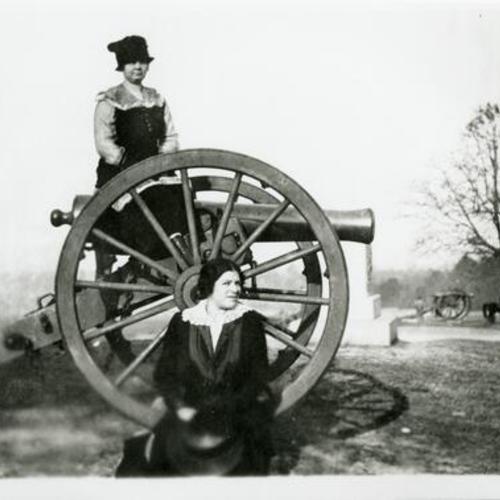 [Portrait of two women next to and on a cannon at a park or cemetery]