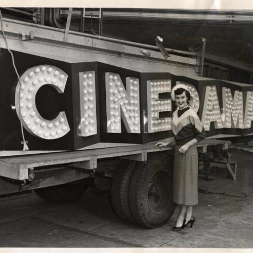 [Mrs. Allen Schumacher standing in front of the new "Cinerama" sign that was replacing the old "Orpheum" sign after a name change at the Market Street theater]