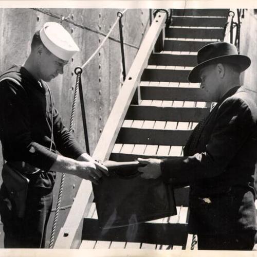 [Coast Guard crewman inspecting a package belonging to a man boarding a ship at the San Francisco waterfront]