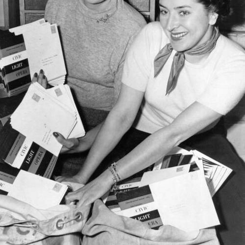[Dorothy Sullivan and Dolores Packard pose with mailing sacks filled with ticket blanks and brochures for the Civic Light Opera Festival at the Curran Theater]