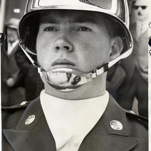 [Army color guard standing during ceremony with anti-war slogan reflection on helmet]
