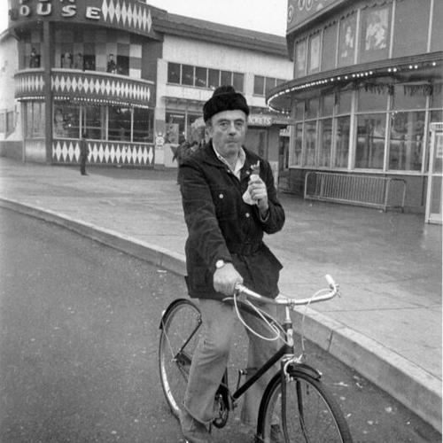 [Unidentified man sitting on a bicycle and eating an ice cream cone at Playland at the Beach]