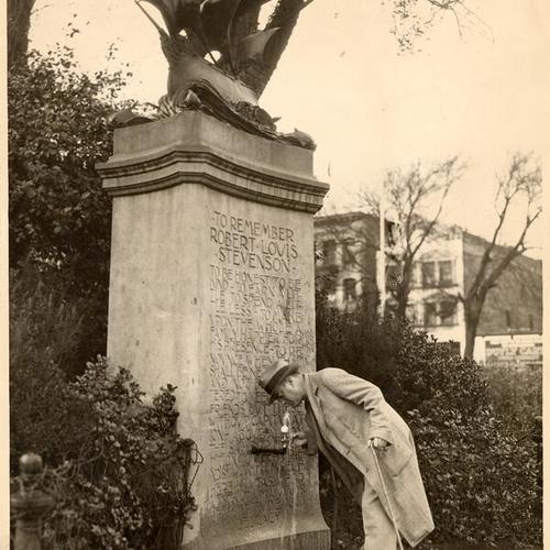 [Man drinking from water fountain on Robert Louis Stevenson monument]
