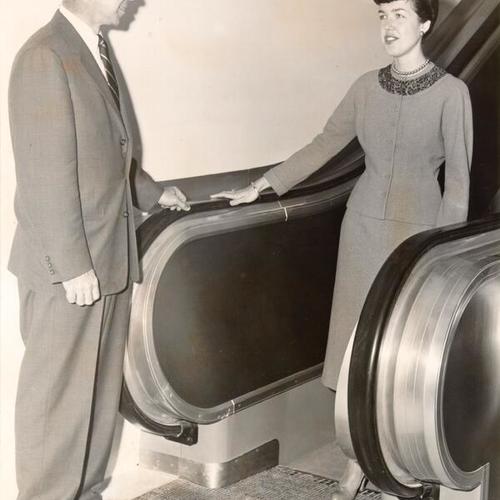 [M. H. DeVoto, general merchandise manager for The Emporium, watching store employee Anne Mero take the first ride on a newly installed escalator]
