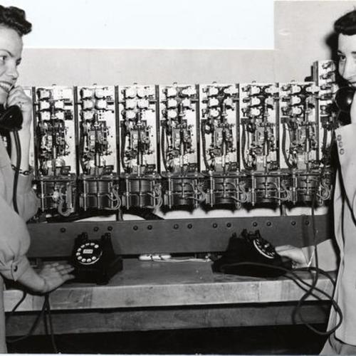 [Marjorie Bennetts and Daphne Davis posing with equipment used to teach people how to operate a dial telephone]