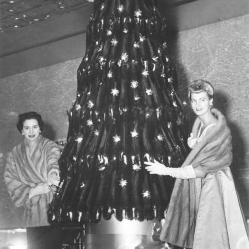 [Jane Winter and Evelyn Hakala standing next to a mink skin Christmas tree at I. Magnin]