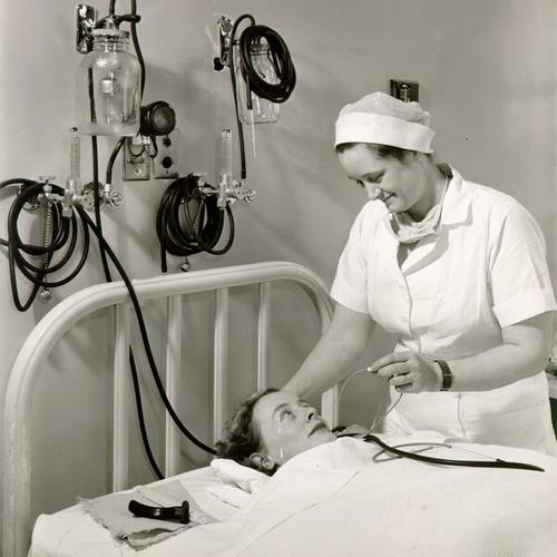 [Anaesthetist Cecelia Davis and student nurse Jane Van Eppuen demonstrating equipment available to patients in the surgical recovery room at Franklin Hospital]